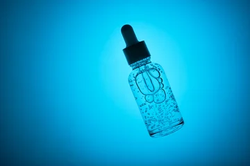 Dropper bottle filled with serum, displaying bubbles and pipette on blue background © colnihko
