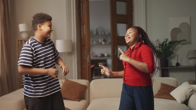 Two carefree African American siblings dancing and singing at home