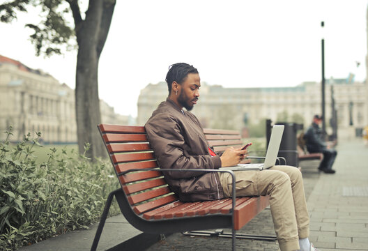 Young man working remotely on a city park bench