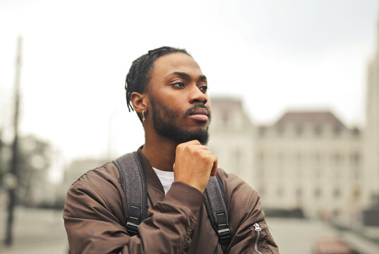 Thoughtful young man with braids standing in a city