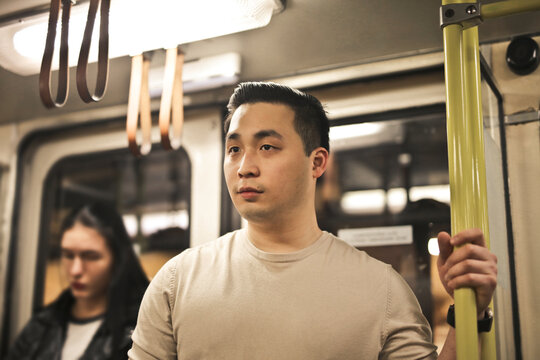 Young Asian man holding a pole on public transportation