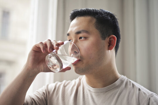 Asian man drinking a glass of water at home
