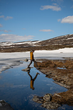 Hiker crossing meltwater beside partially frozen lake in Lapland