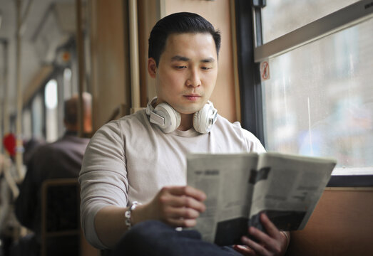 Asian man reading a newspaper on public transit