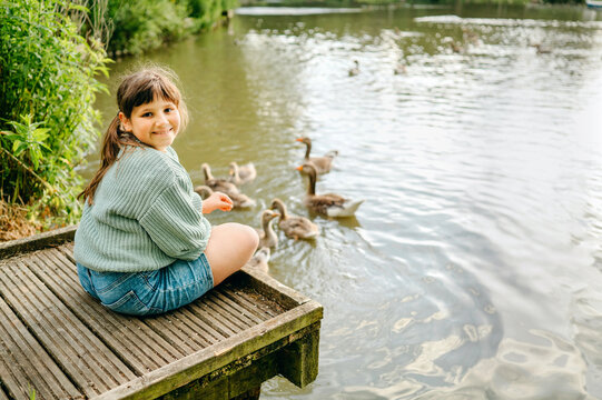 Smiling child sitting on a dock surrounded by waterfowl