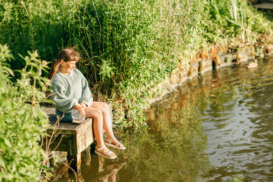 Girl sitting by a lakeside in England surrounded by summer greenery
