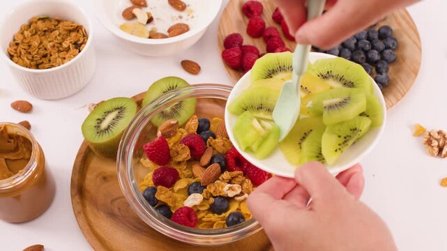 Hands Adding Fresh Sliced Kiwi to a Healthy Breakfast Cereal Bowl