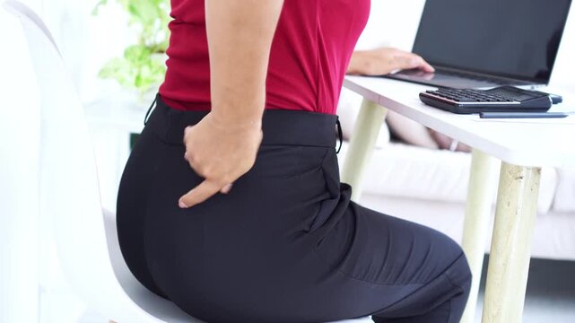 Close-up of a businesswoman suffering from lower back pain while working at her desk. Female office worker holding her painful waist due to office syndrome ,Sciatica and long hours sitting