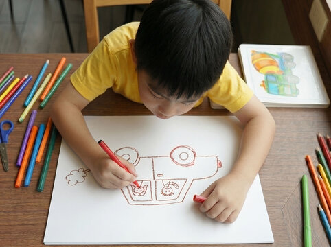 High angle view of Cute Asian boy drawing a car with colored markers on white paper on a wooden table,art education concept.