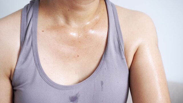 close-up of a sweaty woman in grey athletic wear with sweat drops on her chest and neck after an intense workout, representing fitness dedication, calorie burning, and healthy skin at home