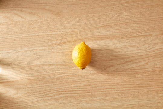 Single fresh yellow lemon on light wooden background
