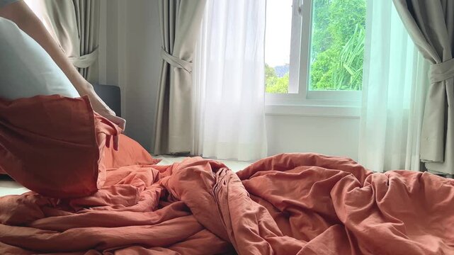 Woman removing bed linen and pillowcase from a bed for washing, everyday laundry and housekeeping routine in a bright bedroom
