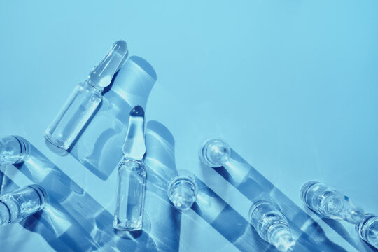 Ampoules containing clear liquid medicine casting strong shadows on blue surface