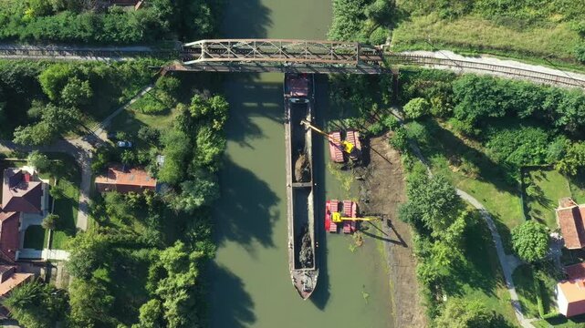 Above top view, dolly move downward over two excavators dredge as dredging, work on river, canal, deepening and removing sediment, mud from riverbed in a polluted waterway near old railroad bridge.