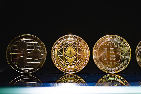  Monedas f&iacute;sicas Ripple XRP،Ethereum ETH y Bitcoin BTC alineadas en fila sobre una superficie reflectante azul. Imagen editorial de tres monedas de criptomonedas principales para clasificaci&oacute;n