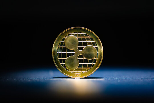  Moneda f&iacute;sica Ripple XRP de oro simple en posici&oacute;n vertical sobre una superficie reflectante azul oscuro،imagen editorial de la moneda de criptomoneda Ripple XRP para noticias sobre el precio de XRP