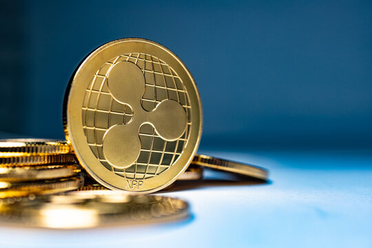  Primer plano de la moneda f&iacute;sica Gold Ripple XRP apoyada en la pila de monedas sobre una superficie reflectante azul, primer plano editorial de la moneda Ripple XRP para noticias