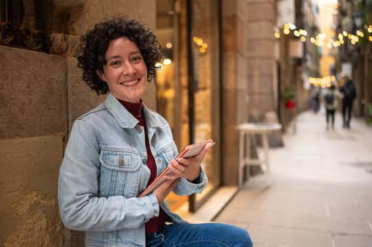 Curly hair woman smiling using digital tablet in urban street
