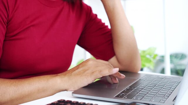 close-up side view of a woman in a red shirt typing on a laptop keyboard at a white desk, focusing on remote work, online learning, digital communication, home office tasks, and business blogging