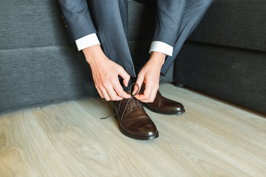 Groom in a blue suit tying the laces on his classic brown leather shoes.