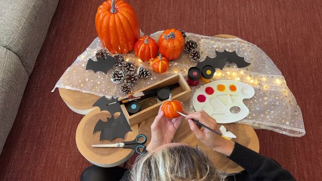 Dolly out cenital de mujer pintando calabaza decorativa Halloween