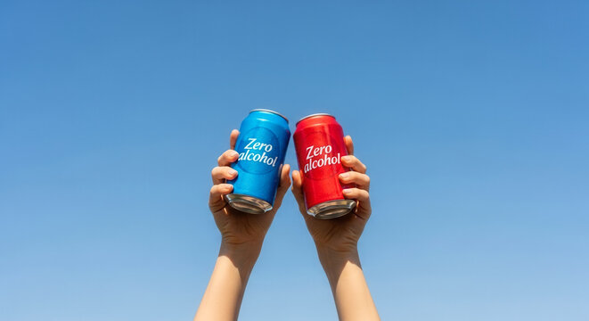 Hands holding up a Zero alcohol drink can in blue and red variations, symbolizing healthy refreshment and sober choices under a blue sky.