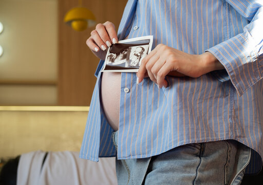 Pregnant woman is holding ultrasound photo near belly