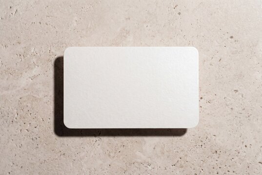 Blank luxury business card with rounded corners floating above travertine stone surface, premium paper mockup copy space