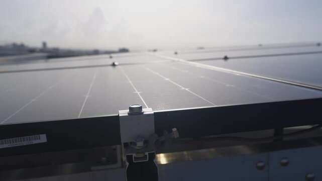 Close-up tracking shot of a modern rooftop solar panel array, revealing the mounting hardware and modular design with an urban cityscape in the background