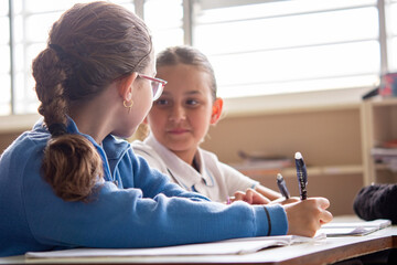 Fototapeta premium Elementary School Girls Studying and Talking Together in Classroom