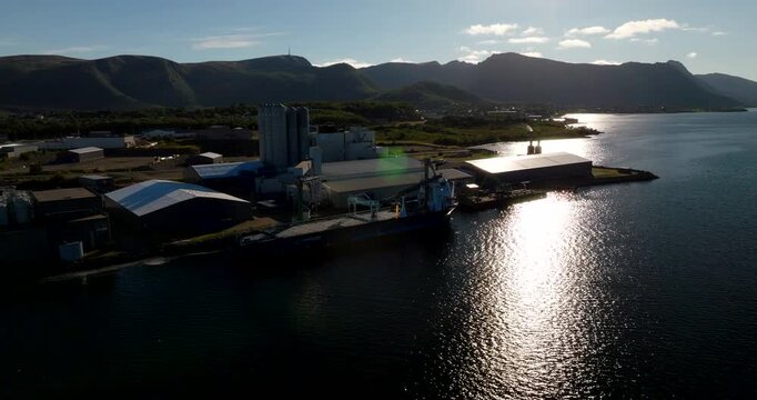Drone view of coastal industrial park with large silos and cargo ship docked at pier in Stokmarknes, Norway. Aerial, copy space