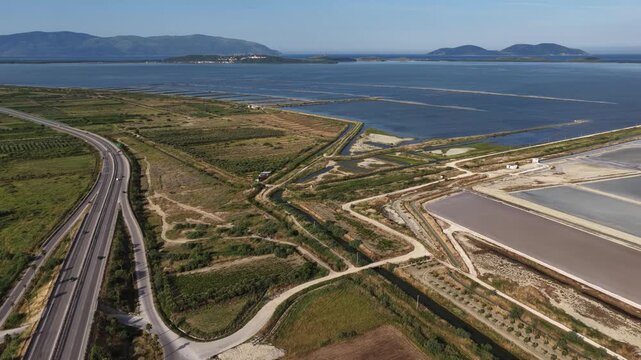 Aerial view of the Narta Lagoon salt pans and the A2 motorway winding through green fields under a clear blue sky in Vlore, Vlore County, Albania.