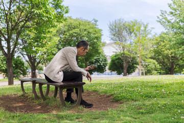 Fototapeta premium 公園のベンチでスマートフォンを見る日本人男性