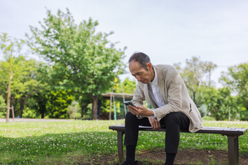 Obraz premium 公園のベンチでスマートフォンを見る日本人男性