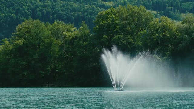Water fountain sprays across the calm waters of Walensee, Switzerland, surrounded by lush forested shores. Serene lakeside scene showcasing natural beauty and tranquil outdoor atmosphere.
