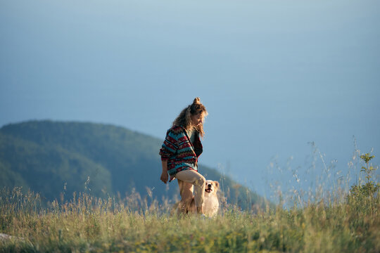 A woman sits with her Border Collie above scenic mountain scenery and open sky. Peaceful atmosphere creates travel and outdoor lifestyle inspiration.