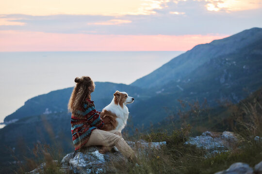 A woman relaxes with her Border Collie on a scenic mountain viewpoint above the coastline. Peaceful atmosphere creates outdoor lifestyle and adventure feeling.