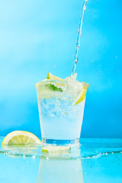 Fresh cold water pouring into a glass with lemon and lime slices on blue background