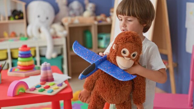 Boy hugging a large stuffed monkey while holding a foam airplane by a colorful toy table in a playroom inside a building; joyful play.