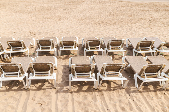 Rows of empty sun loungers arranged on sandy beach at Mediterranean seaside resort