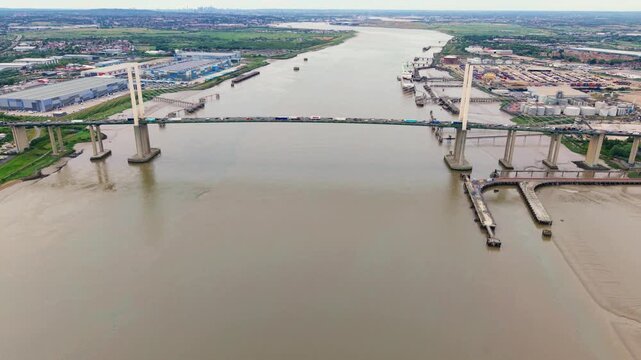 Aerial view of the Queen Elizabeth II Bridge crossing the River Thames with industrial warehouses and shipping containers on the banks in Dartford, England, United Kingdom.