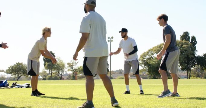 Passing small red ball, diverse friends in sportswear forming semicircle on park lawn, bats