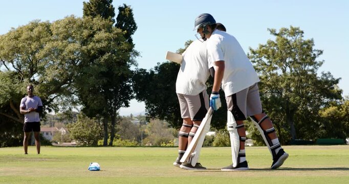African american male batter celebrating fifty raising bat, adjusting helmet on field