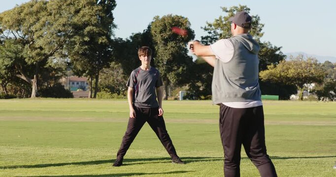 Diverse male friends practicing on field, bowler bowling batsman swinging bat
