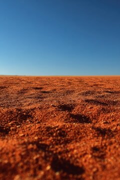 Endless bright red desert sand under a clear deep blue sky background minimal landscape, closeup of small orange dunes grains with texture in sharp focus and copy space for travel concepts