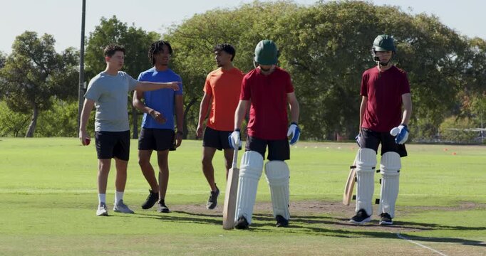 Stepping onto marked pitch, diverse cricket teammates warming up for bowling practice at park