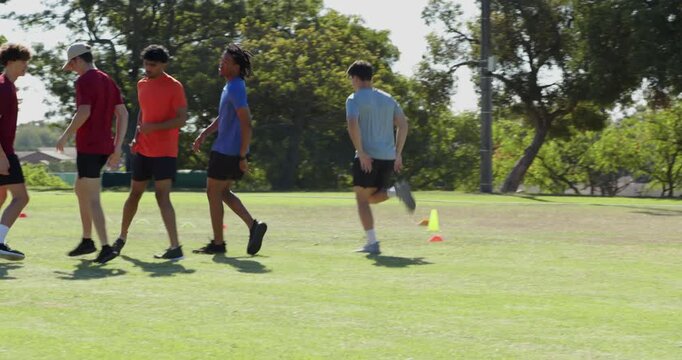Diverse male team spotting cones initiating high-knee butt-kick drills on grass for training