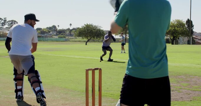 Cricket teammates training bowler jogging batsman blocking ball, keeper collecting, copy space
