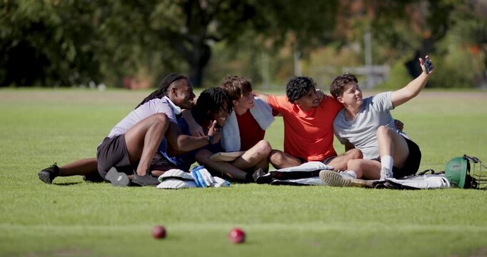 Diverse male friends in park using smartphone selfie, reviewing shot pointing bocce balls