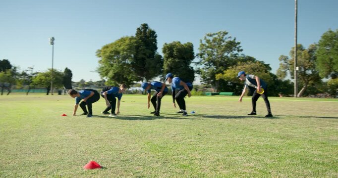 Practicing teenage male team crouching on park field, using red and blue cones, yellow disc